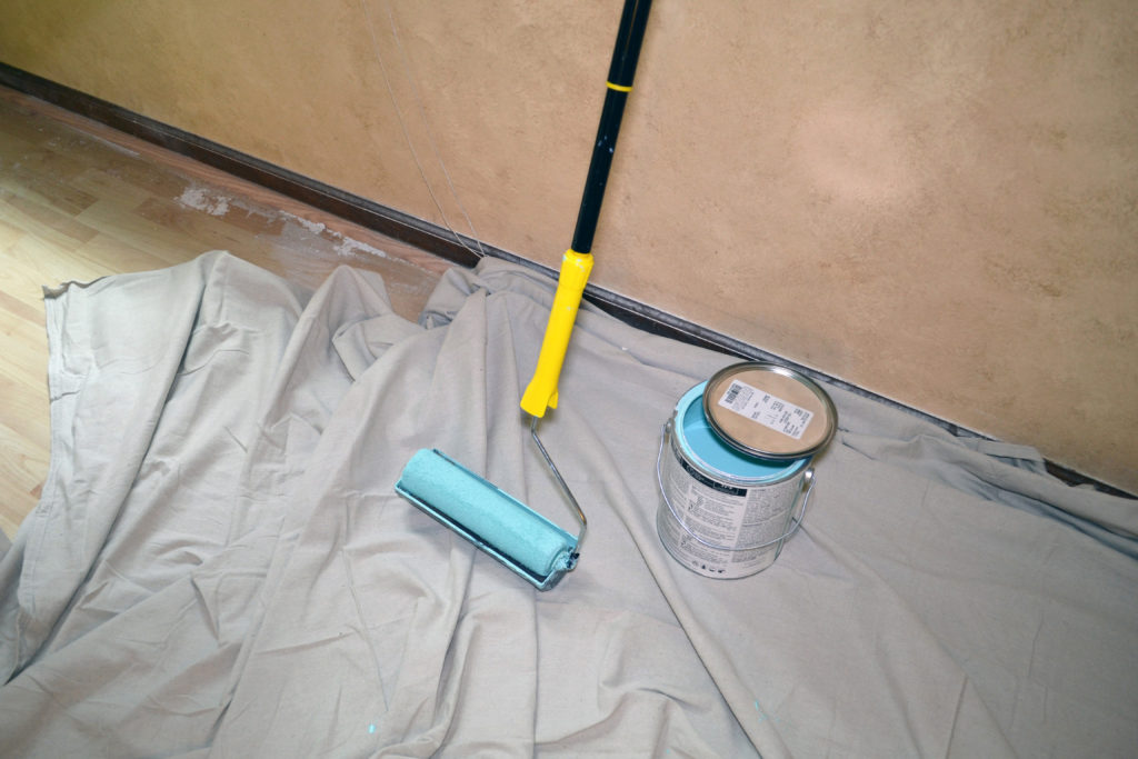 Smart Painter pole leaning against a wall next to a can of paint.